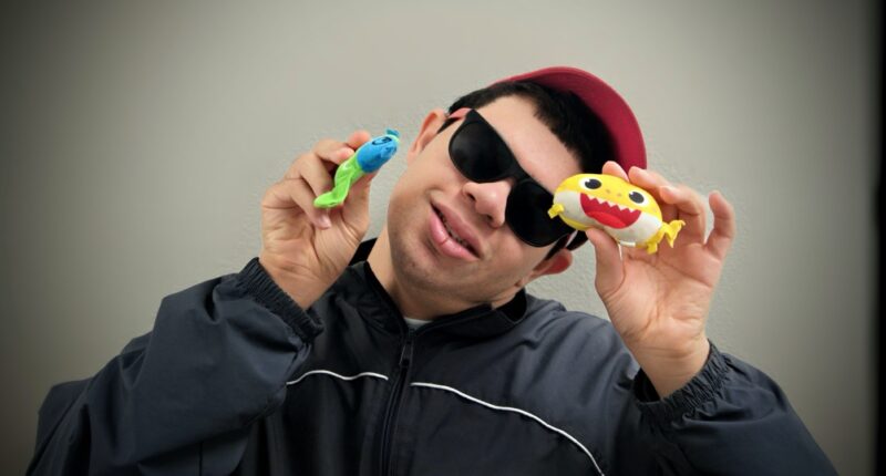 Clubhouse member wearing sunglasses and a cap, smiling while holding two colorful toy figures