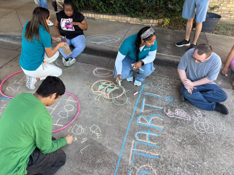 Clubbers and staff draw with chalk together on a driveway